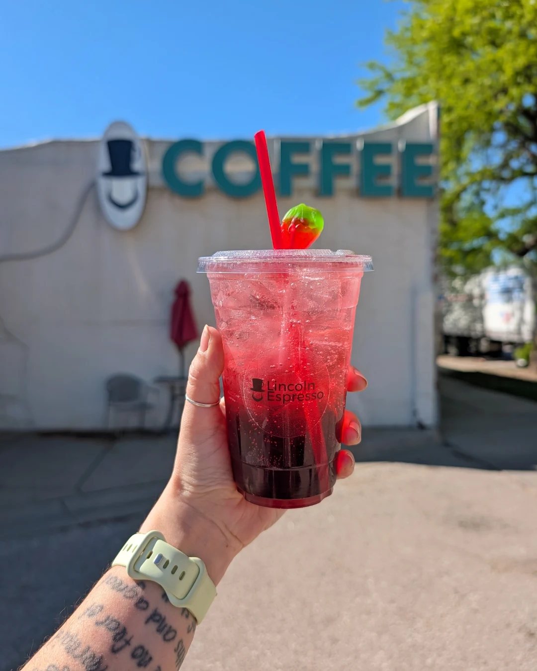 A Lotus energy drink held up in front of the Lincoln Espresso sign